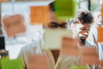 Multiracial business team brainstorming, discussing and planning in a modern office. Glass board covered with sticky notes represents their progress and strategies.