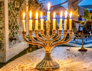 Fototapeta premium Happy Hanukkah with a glowing menorah at night next to a Torah scroll and a Bible, open Torah in the candlelight of the menorah