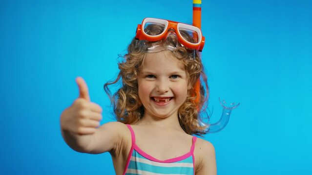 Cute curly girl with a swimming mask and snorkel is showing big thumb