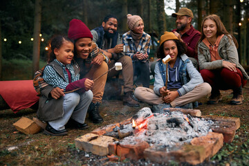 Happy people roasting marshmallows on fire while camping in nature.