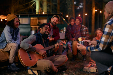 Happy black man plays acoustic guitar while enjoying with friends on camping.