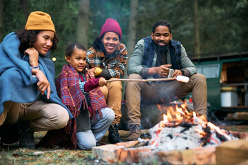 Happy black family roasting marshmallows while camping in woods.