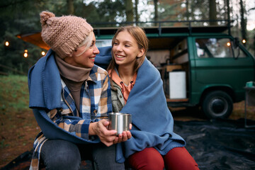 Happy mother and daughter talk while relaxing at camper trailer park. - obrazy, fototapety, plakaty