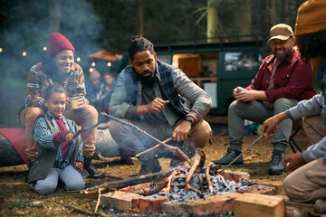 Multiracial family friends enjoying by bonfire at camper trailer park.