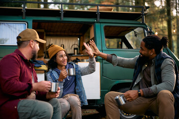 Happy black father and son giving high five while camping with their family friend in nature.