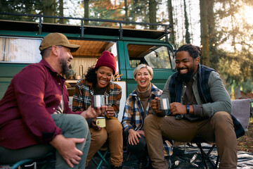 Multiracial cheerful friends have fun by camper trailer in woods.