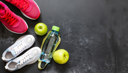 Fitness concept with red sneakers dumbbells pomelo bottle of water apple and measure tape on black...