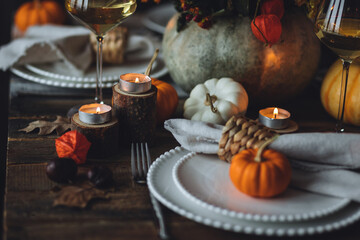 Cozy festive holiday table decor for home family Thanksgiving dinner. Traditional event, elegant natural decoration. Wooden rustic table, countryside style. Burning candles, floral centrepiece pumpkin