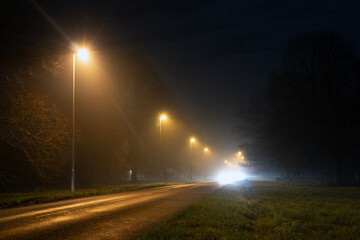 A long straight road with street lights, glowing on a misty winters night in the countryside with...