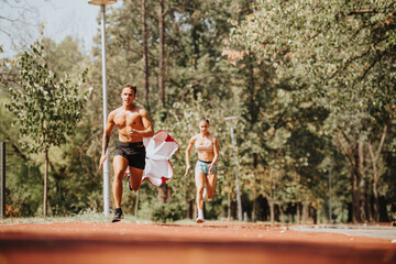Fit couple sprinting with a parachute in a sunny park. They train together, motivated by positive results. Natural environment enhances their outdoor workout.