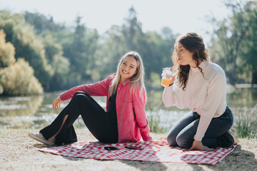 Two young women have a carefree conversation in a sunny city park surrounded by nature. They radiate positivity and happiness while socializing and enjoying their time together.