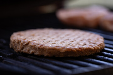 Close up of frozen beef burger patty placed on the barbecue for grilling
