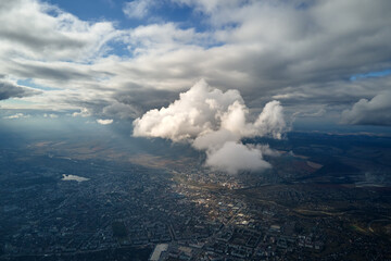 Aerial view from airplane window at high altitude of distant city covered with white puffy cumulus clouds