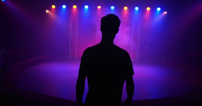 Slow-motion a person's silhouette walking to an empty  concert stage with red and blue lights