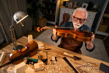 Senior carpenter craftsman carving wood and making violin instrument - obrazy, fototapety, plakaty
