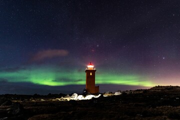 Majestic lighthouse stands on a rocky shoreline, illuminated by an ethereal light of an aurora