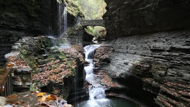 water flowing at rainbow falls in watkins glen state park (waterfall, scenery, finger lakes region of new york state) beautiful autumn hiking trail with bridge and staircase inside gorge (cascade)