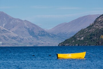 Closeup of a small yellow sailboat n a serene body of water, with mountain peaks in the background
