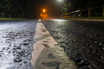 A low angle shot of an empty road on a misty night with street lights and a shallow depth of field.
