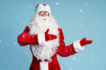 Funny Saint Nicholas or Santa Claus pointing with hands on blue background, snow. Winter holidays concept 