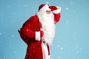 Santa Claus holding bag with gifts looking away,  hurry up isolated on blue background with snow, copy space. Holidays, advertisement concept 