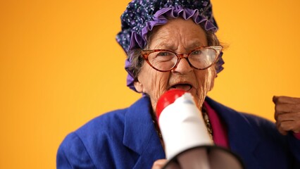 Closeup portrait of funny toothless old elderly senior crazy grandmother woman yelling cheering into megaphone bullhorn announcing something isolated on yellow background.