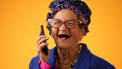 Closeup of funny crazy happy elderly old toothless woman talking on mobile cell phone wearing...