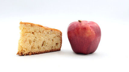 closeup of a slice of homemade apple pie with a red apple next to it on a white background