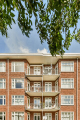 Fototapeta premium a brick apartment building with balks on the balcony and green trees in the fore - swayr stock photo