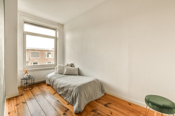 a bedroom with wood flooring and a bed in the corner, next to a window that looks out onto the...