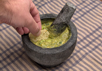 hand dipping tortilla chip into guacamole inside molcajete (traditional mexican mortar and pestle...