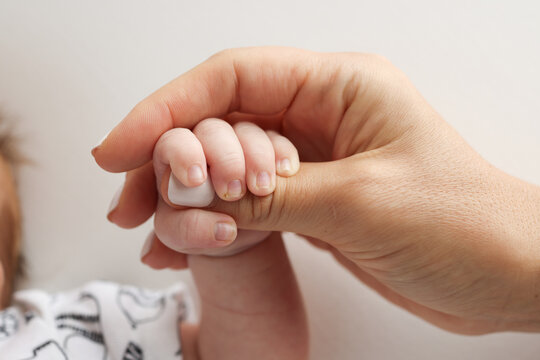 Parents' hands hold the fingers of a newborn baby. The hand of a mother and father close-up holds the fist of a newborn baby. Family health and medical care. Professional photo on white background