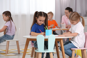 Group of cute little children and nursery teacher drawing at desks in kindergarten. Playtime activities