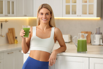 Happy woman with glass of fresh celery juice in kitchen