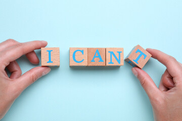 Motivation concept. Woman changing phrase from I Can't into I Can by removing wooden cube with letter T on light blue background, top view - obrazy, fototapety, plakaty
