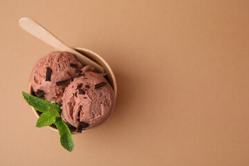 Paper cup with tasty chocolate ice cream, sticks and mint leaves on light brown background, top view. Space for text