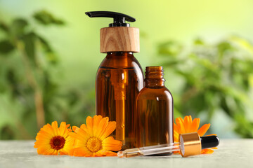 Bottles of essential oils and beautiful calendula flowers on white table outdoors, closeup