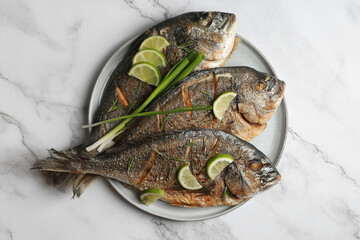 Delicious baked fish served with green onion and lime on white marble table, top view. Seafood