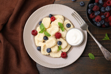 Plate of tasty lazy dumplings with berries, sour cream and mint leaves on wooden table, flat lay