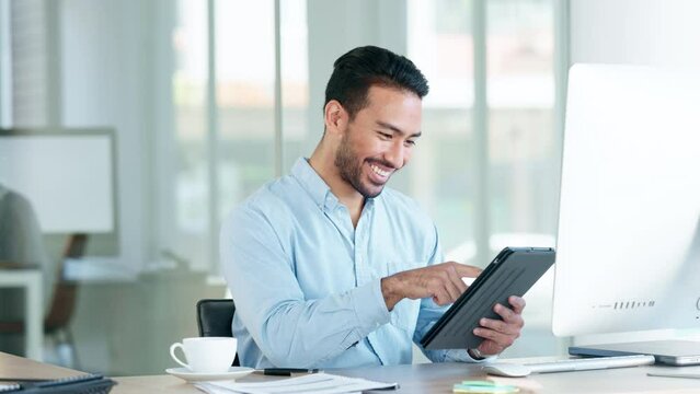 Happy accountant browsing the internet on a tablet and sitting in an office. Male financial advisor laughing at social media clickbait from his workplace. Stock broker smiling at funny internet posts