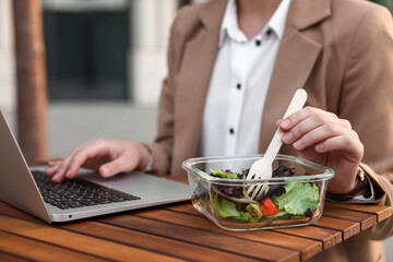 Businesswoman using laptop during lunch at wooden table outdoors, closeup
