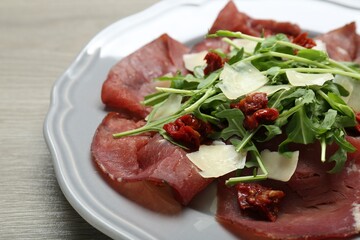 Plate of tasty bresaola salad with sun-dried tomatoes and parmesan cheese on wooden table, closeup