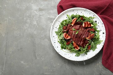 Plate of tasty bresaola salad with figs, sun-dried tomatoes and balsamic vinegar on grey table, top view. Space for text