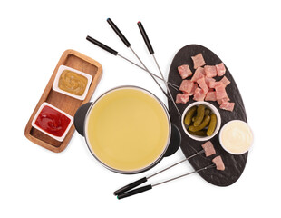 Oil in fondue pot, forks, pickles, sauces and pieces of raw meat isolated on white, top view