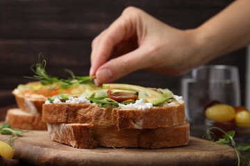 Woman putting microgreens on tasty vegan sandwich with avocado and tomato at table, closeup