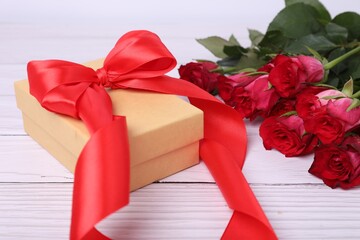 Gift box with red bow and bouquet of beautiful roses on white wooden table, closeup