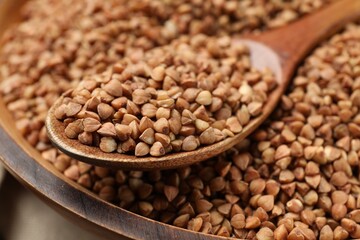 Spoon with dry buckwheat in wooden bowl, closeup