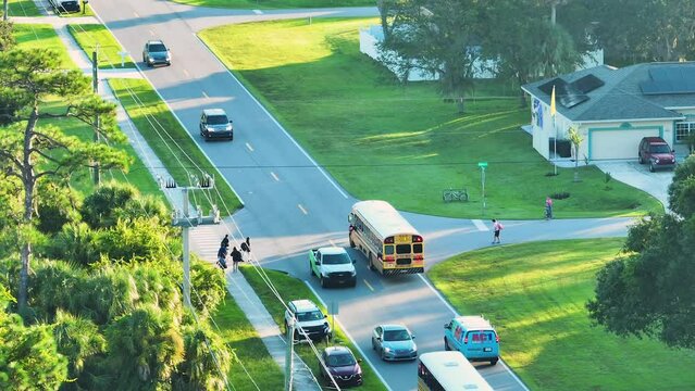 Aerial view of American yellow school bus picking up children at sidewalk bus stop for their lessons in early morning. Public transportation in the USA