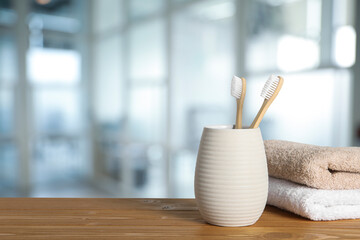 Bamboo toothbrushes in holder and towels on wooden table against blurred background, space for text