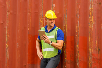 Caucasian man wearing yellow safety helmet Wear a reflective safety suit, hold a tablet, and stand smiling against a container. In the container storage yard